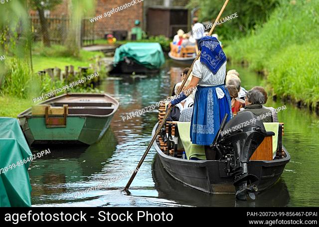 16 July 2020, Brandenburg, Schlepzig: A barge ferrywoman wears a Sorbian-Wendish working costume and drives tourists in a barge over a river