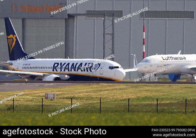 22 May 2023, Berlin, Schönefeld: A Boeing 737 (l) of the airline Ryanair taxis for takeoff behind a green field at Berlin Brandenburg Airport (BER) ""Willy...