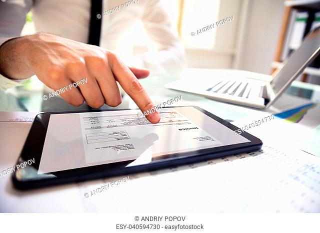 Close-up Of A Businessperson's Hand Analyzing Bill On Digital Tablet Over Desk