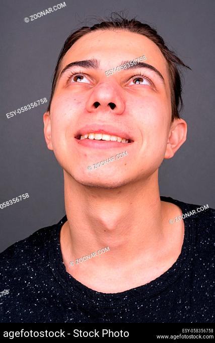 Studio shot of young handsome androgynous man with long hair against gray background