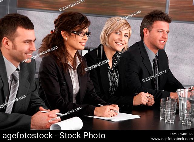 Attractive young businesswoman sitting at table on business seminar together with colleagues, looking at camera, smiling