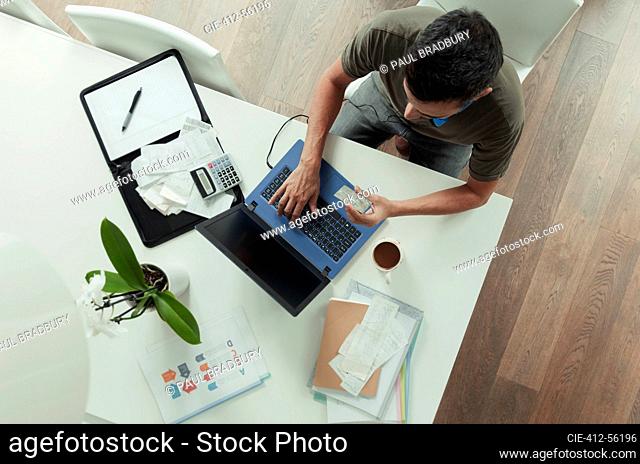 Man with credit card paying bills at laptop on dining table