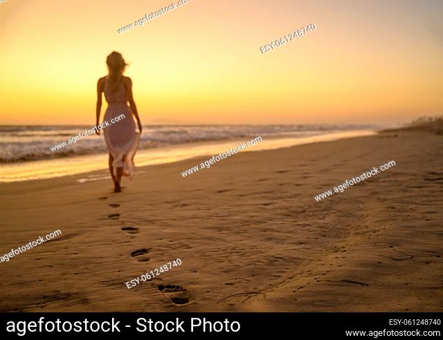 She has gone. Beautiful woman wearing a gorgeous summer clothes and walking away into the sunset somewhere on the cost of the California cost