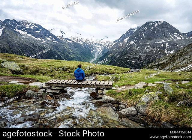 man hiker resting on small bridge over mountaian river at schlegeis lake, zillertal alps, austria