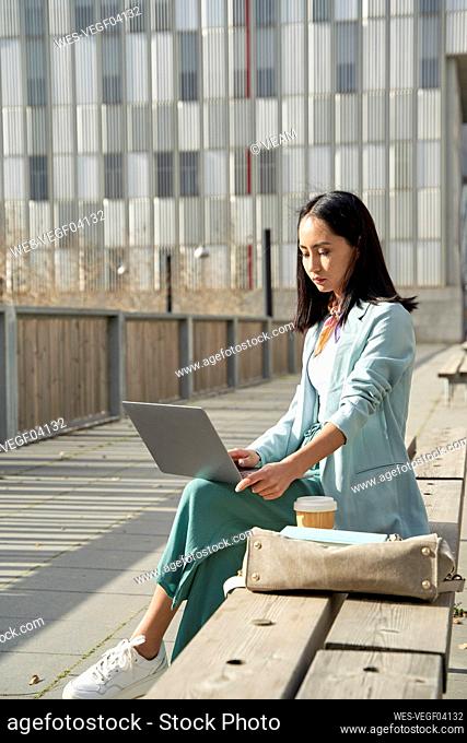 Young businesswoman using laptop while sitting on bench