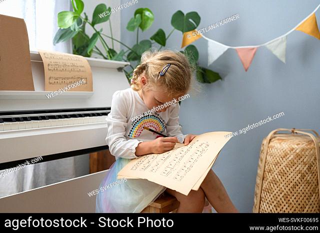 Blond girl writing on musical sheet at home
