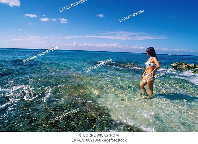 Beach. Young woman in bikini. Standing in clear shallow water