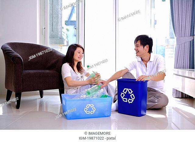 Young couple sitting on the floor and putting empty bottles into the recycling bins