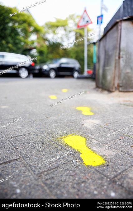 25 August 2022, Lower Saxony, Hanover: Yellow-marked shoe prints have been applied to a sidewalk between the newly established parent stop on Märkischer Weg and...