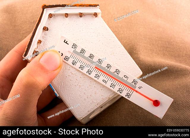 Hand holding a thermometer on a model house
