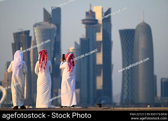 15 December 2022, Qatar, Doha: Men stand on the Corniche boardwalk in front of the skyline with the modern skyscrapers. The World Cup 2022 will end on 18