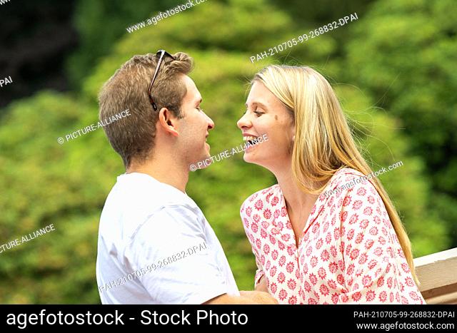 PRODUCTION - 03 July 2021, Lower Saxony, Oldenburg: ILLUSTRATION - A woman and a man are sitting together on a park bench laughing