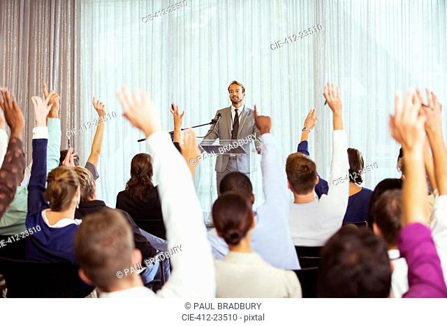 Businessman giving presentation in conference room, people raising hands