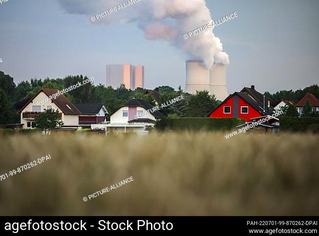 01 July 2022, Saxony, Rötha: The cooling towers of the Lippendorf lignite-fired power plant are steaming behind single-family homes