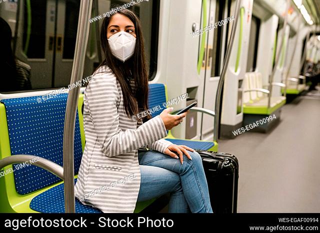Woman looking away while sitting with smart phone in metro train
