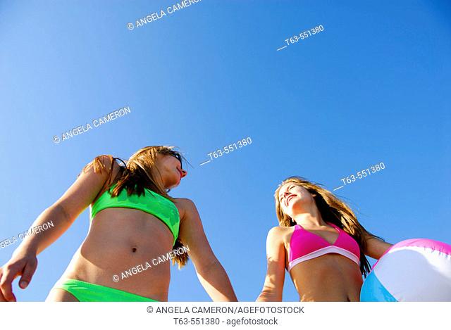 girl 13, girl 18 yrs holding beach ball and holding hands on beach, swimsuits