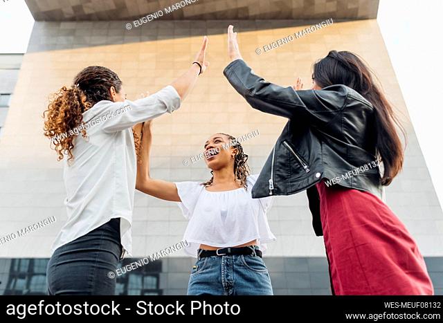 Cheerful multiracial friends doing high-five in front of wall