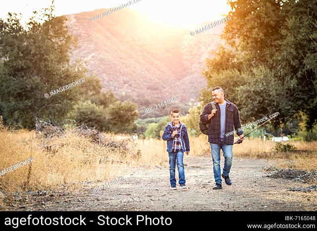 mixed-race father and son outdoors walking with fishing poles