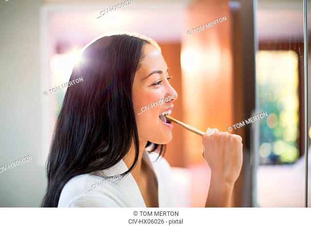 Young woman brushing teeth in bathroom mirror