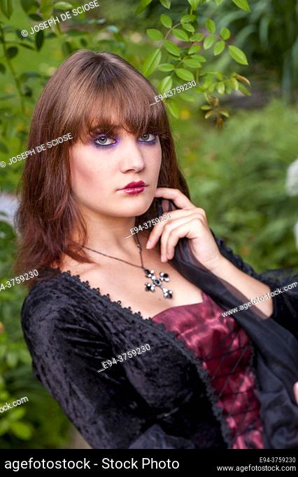 An 18 year old brunette woman wearing a costume in a garden setting looking directly at the camera