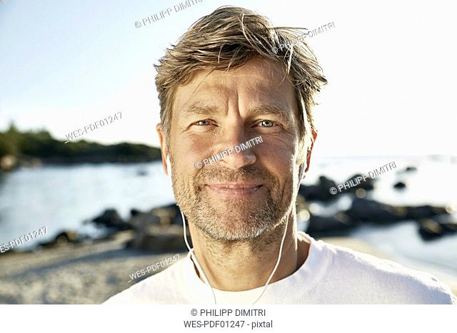 Portrait of confident mature man with earphones on the beach