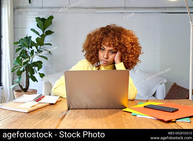 Bored businesswoman with hand in hair working on laptop at home