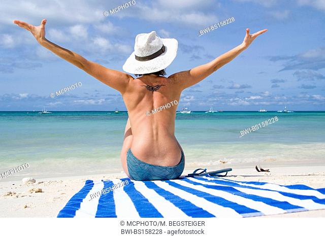 woman with sun hat enjoys the beach holiday, sitting on a striped towel, Philippines