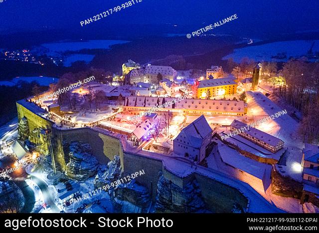 17 December 2022, Saxony, Königstein: Brightly lit are the stalls at the Christmas market on the Königstein Fortress (aerial view with a drone)