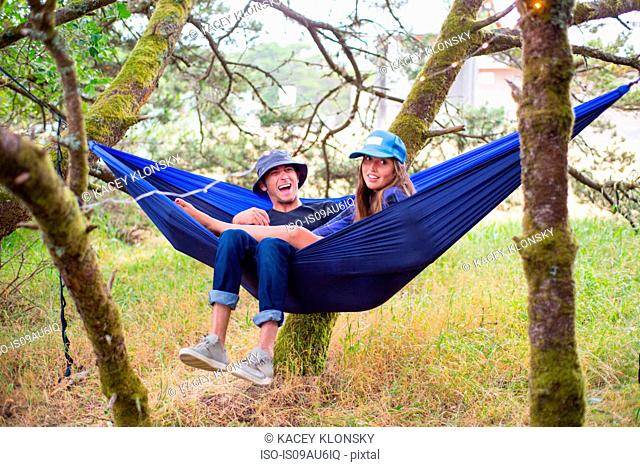 Happy adult couple reclining in blue hammock between trees