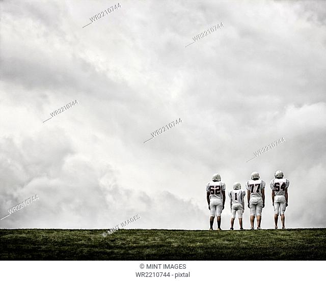 A group of four football players in sports uniform, three tall figures and one shorter team player