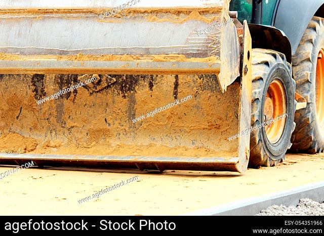 dirty bucket loader worker who works in the town square by moving pallets of paving slabs