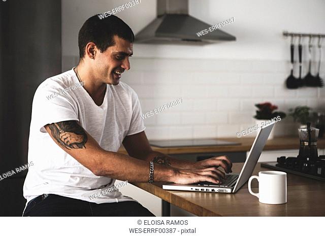 Smiling young man using laptop in kitchen at home