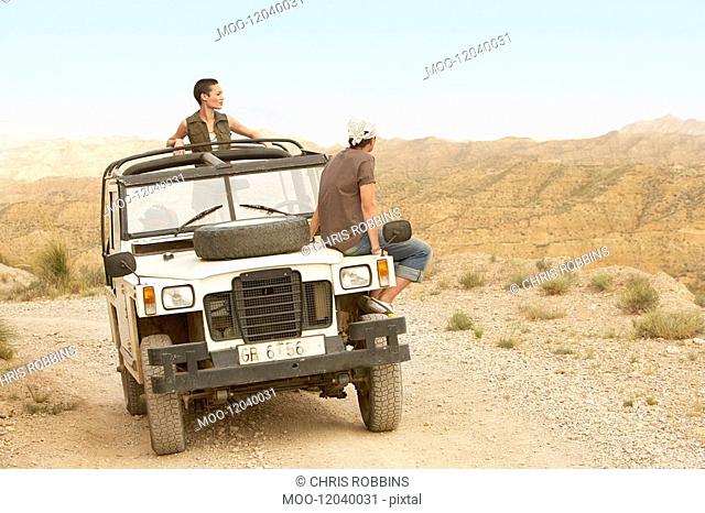 Couple sitting on stationary four wheel drive vehicle in desert