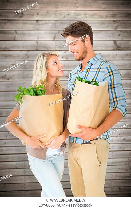 Composite image of attractive couple holding their grocery bags
