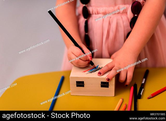 beautiful cute little girl in pink dress painting jewelry box while having fun at home