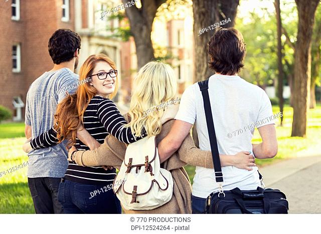 Four friends walking and talking in an embrace on the university campus with a female looking back at the camera; Edmonton, Alberta, Canada