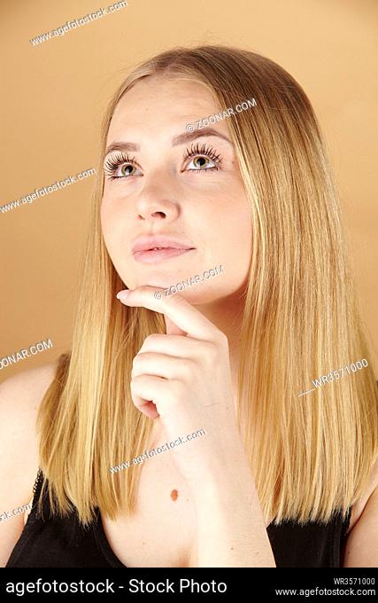 Nachdenkliche blonde junge Frau mit ihrem Finger am Kinn vor braunem Hintergrund isoliert