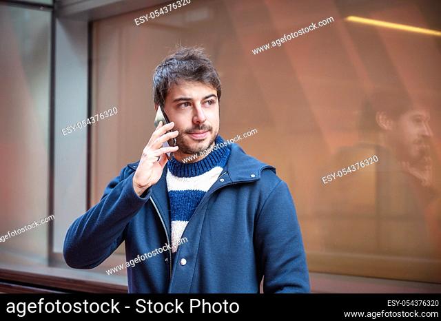Portrait of handsome young man talking on mobile phone on the street, of modern city center. People and technology
