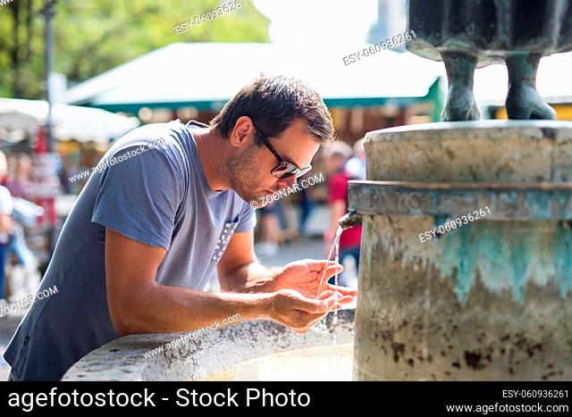 Thirsty young casual cucasian man drinking water from public city fountain on a hot summer day