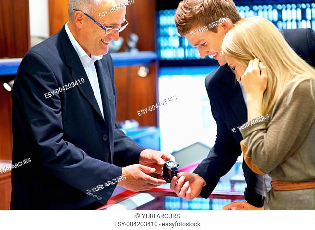 Friendly jeweller showing a wristwatch to an attractive young couple