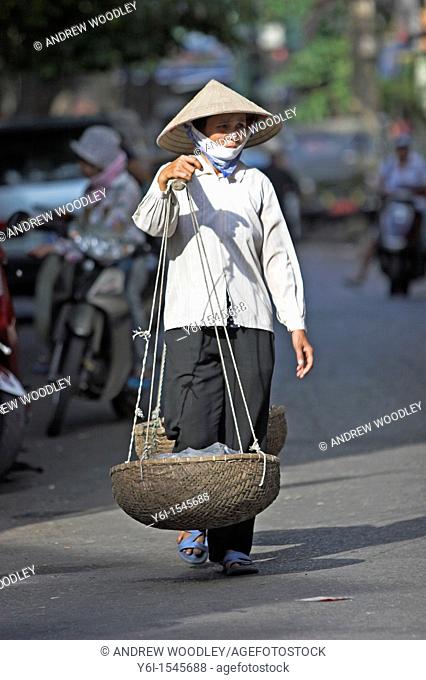 Woman in conical hat carrying shoulder pannier baskets Hanoi Vietnam