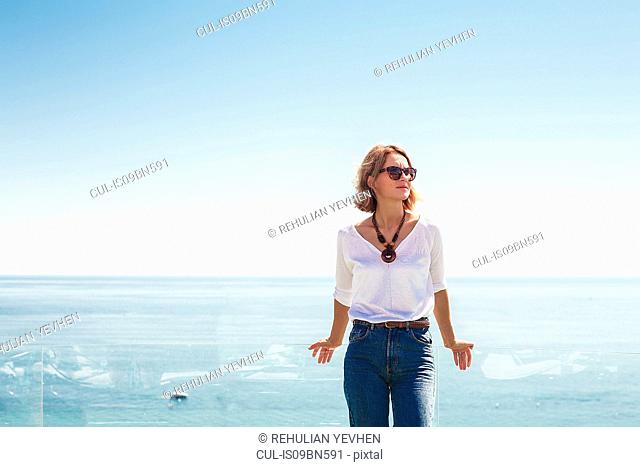 Woman leaning against glass balcony on seaside terrace