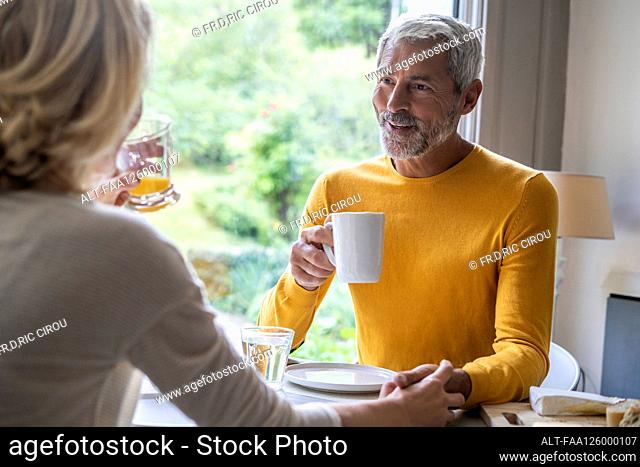 Smiling mature couple holding hands while having breakfast at home