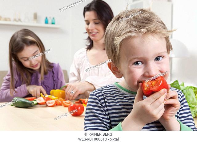 Germany, Bavaria, Munich, Mother and daughter preparing salad, son eating