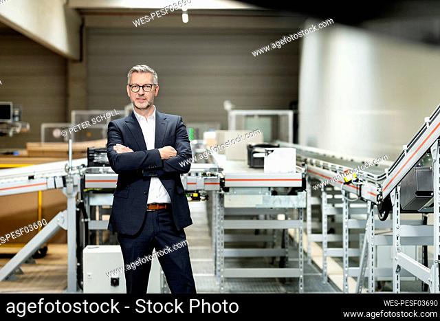 Mature businessman standing confidently with arms crossed in factory