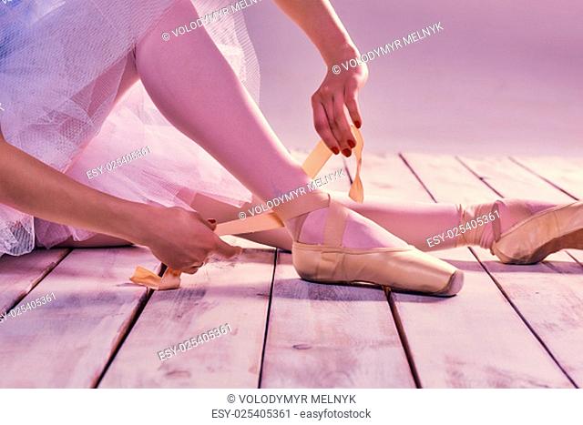 Professional ballerina putting on her ballet shoes on the wooden floor on a pink background. feet close-up