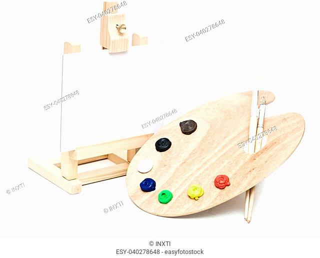 Wooden easel with clean paper and wooden artists palette loaded with various colour paints and brush, isolated on a white background