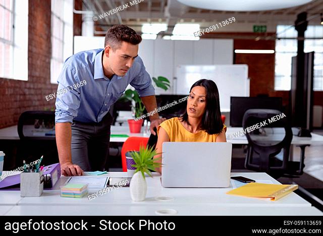 Caucasian male and female business colleague in discussion at desk in office, looking at laptop