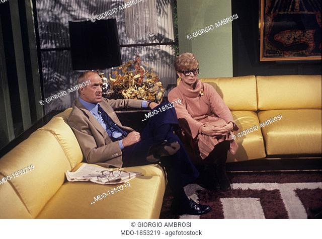 Italian actor and TV host Raimondo Vianello sitting on a sofa beside his wife and Italian actress Sandra Mondaini. They present together the TV variety show Noi...