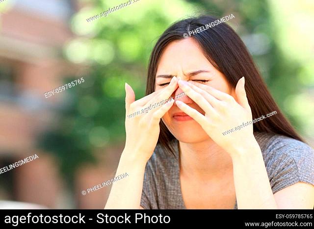 Asian woman scratching itchy eyes in the street